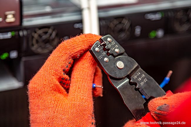 Hände mit orangenfarbenen Handschuhen benutzen eine Crimpzange.