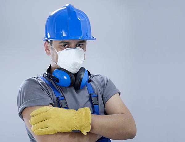 Mann mit Helm, Atemschutzmaske, Ohrenschützer und Handschuhen. Hauptfarbe Blau.